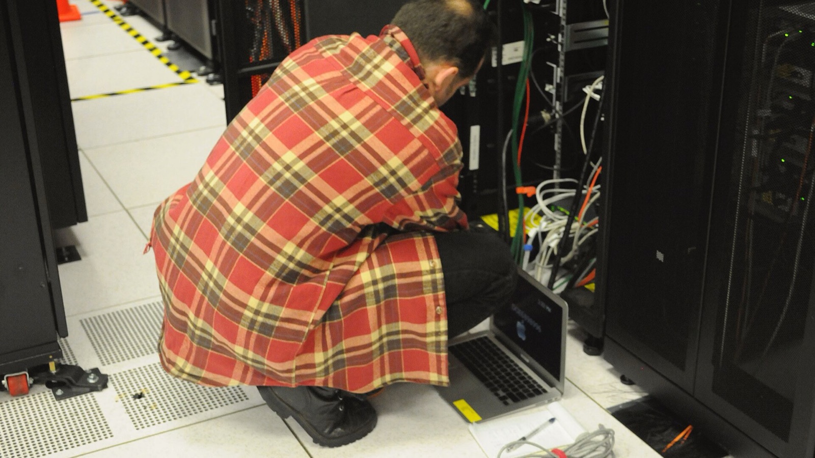 A technician uses a laptop beside an open server rack at NERSC.