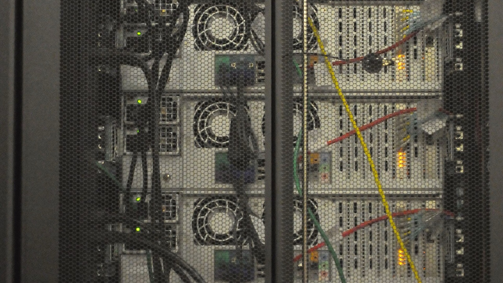 Server cooling fans and network cables behind a perforated rack door at NERSC.